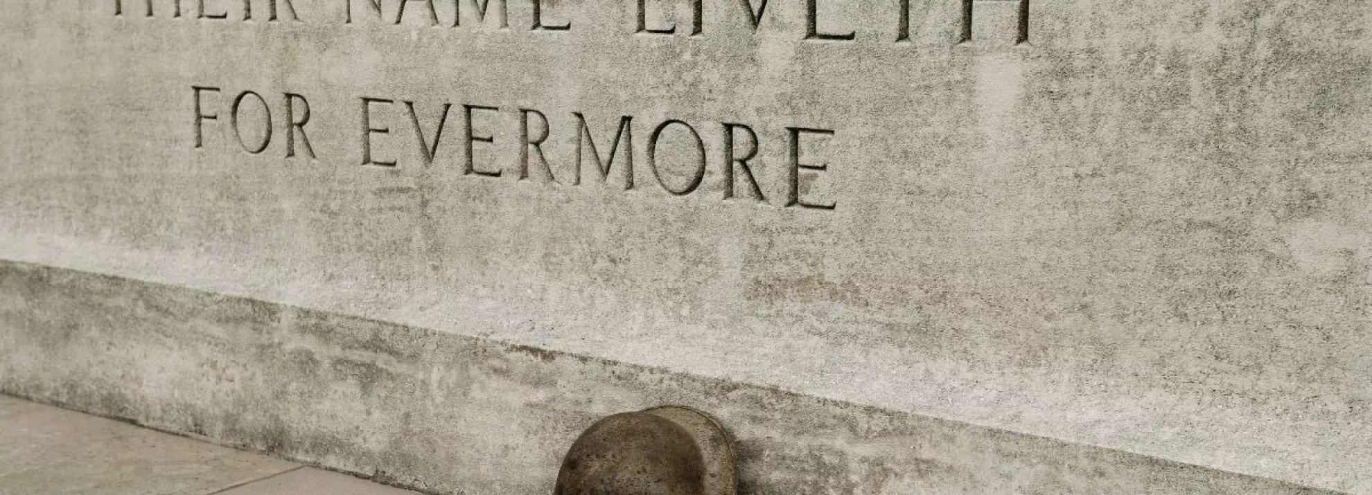 WWI monument with 'their name liveth for evermore' etched into stone with helmet leaning against it