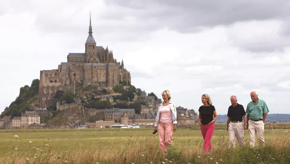 Travelers traversing the field with Mont St Michael in the background.
