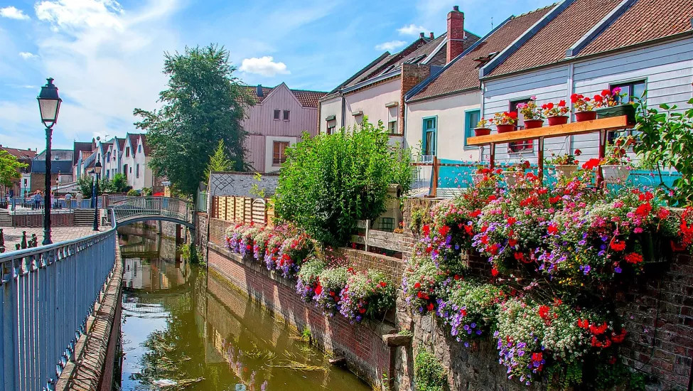 A view of the town of Amiens, with a river flowing through next to flower adorned houses.