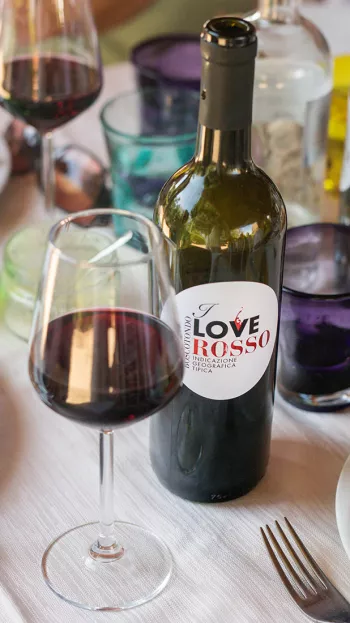 An open bottle of wine and half-full wine glass at a wine tasting.