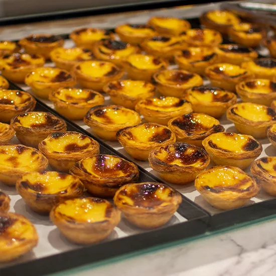 Trays of Pastel de Nata pastries are being prepared for sale.