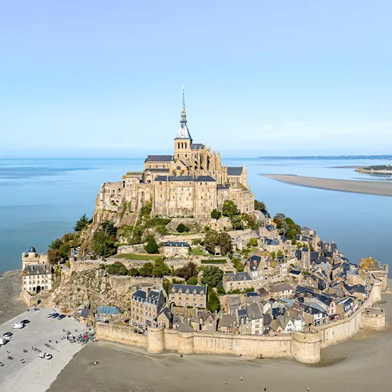 An overhead view of Mont St Michel, a commune with a prominent cathedral at the top surrounded by shifting tides.